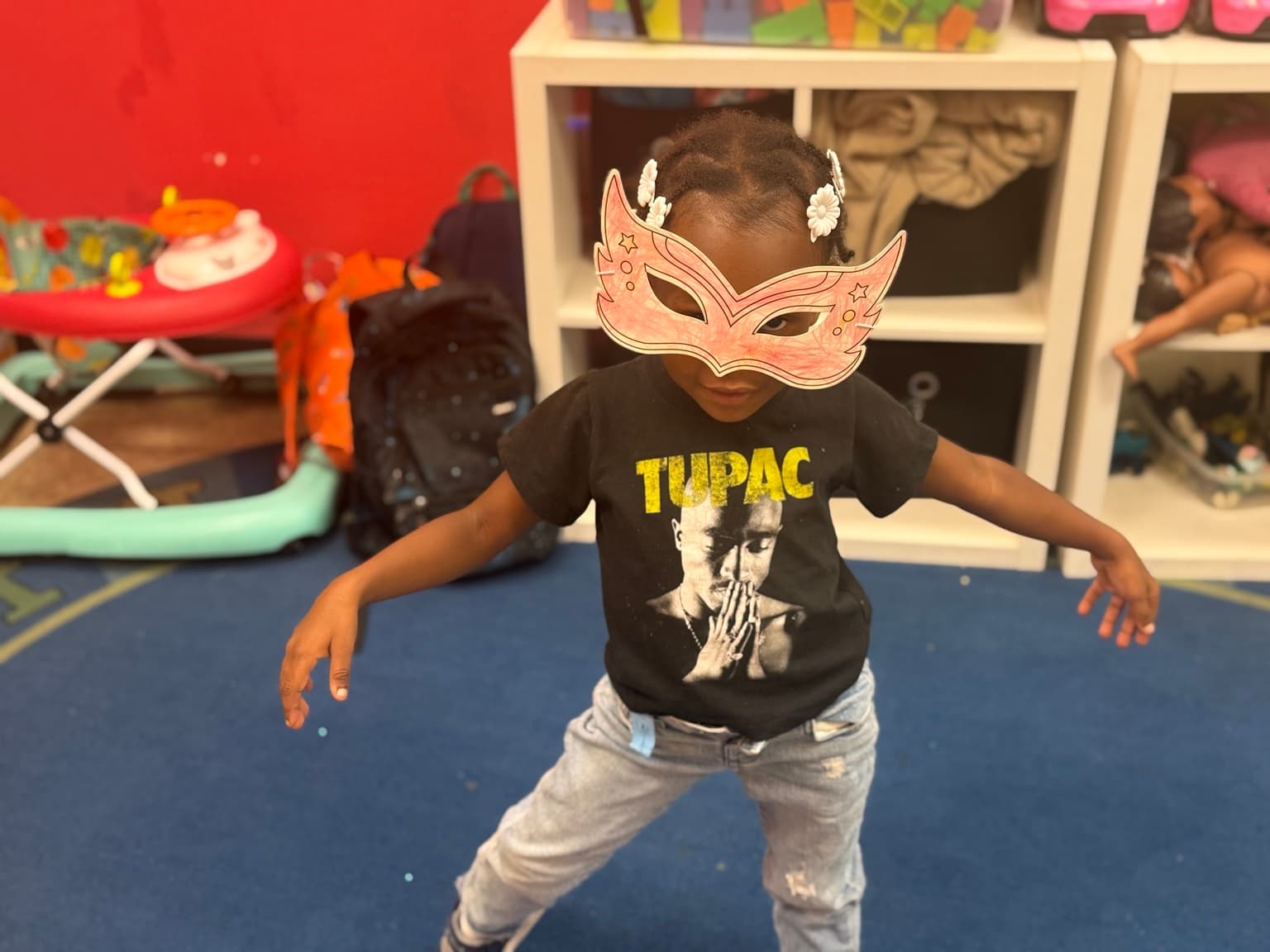A child mid-dance-move wearing a handmade paper mask and a Tupac t-shirt