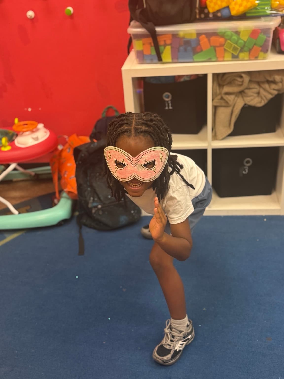 A child striking a superhero pose in a handmade paper mask
