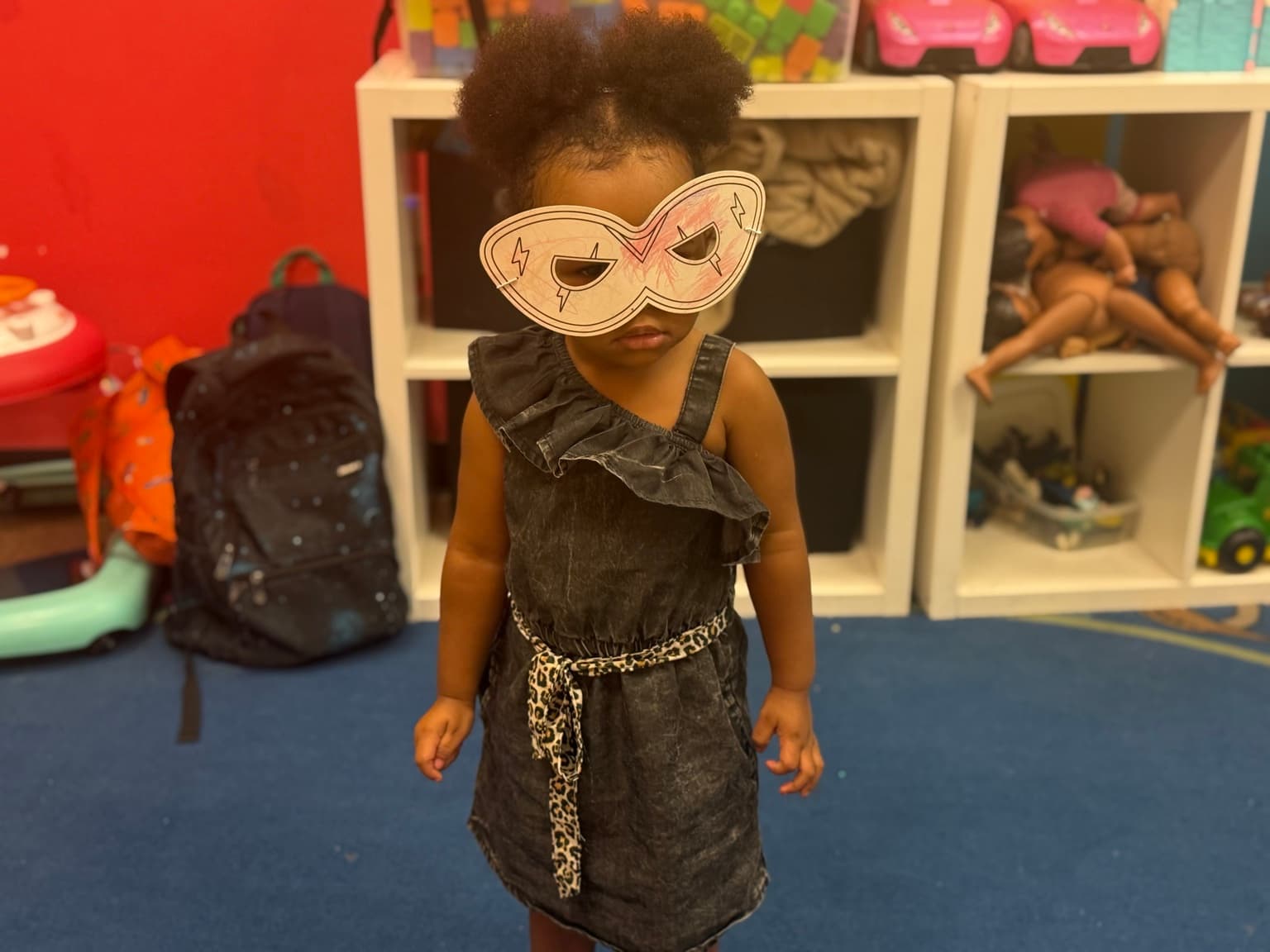 A toddler standing calmly in a handmade paper mask