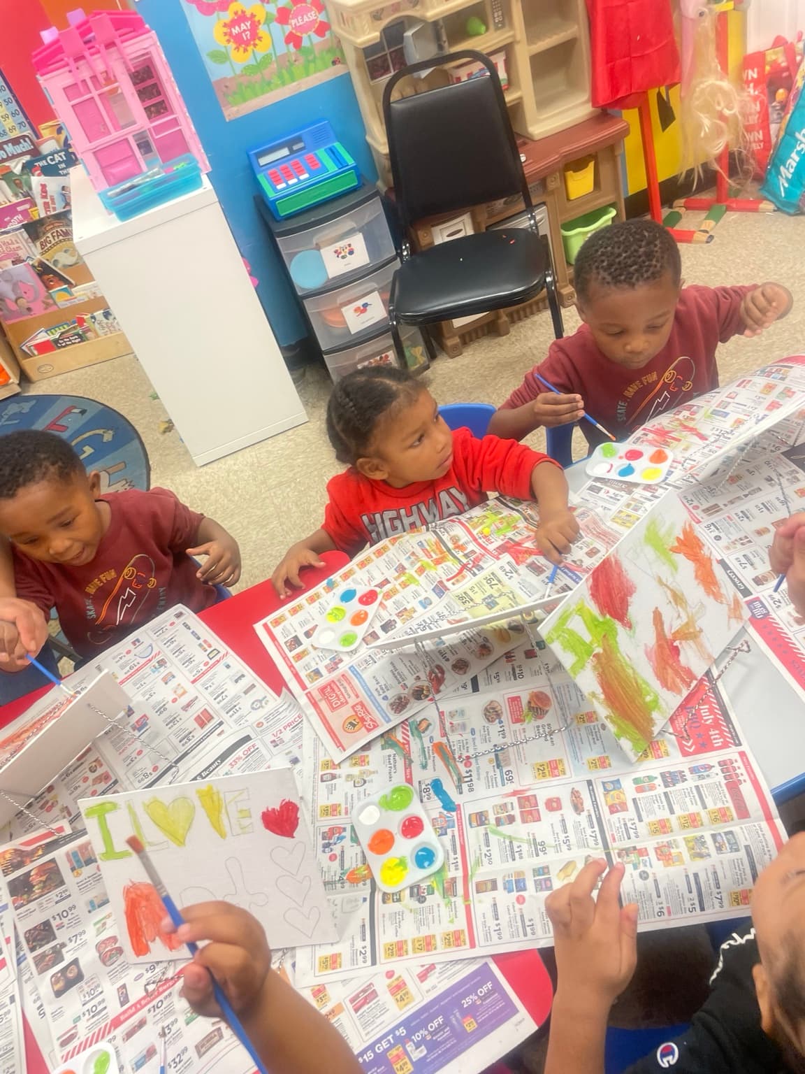 Children painting together at a table covered in newspaper and paint palettes