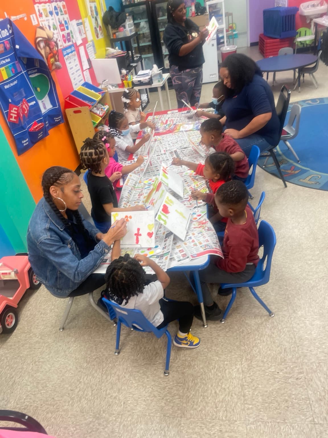 Teachers and children gathered around a long table painting during an art project at Moore Learning Minds