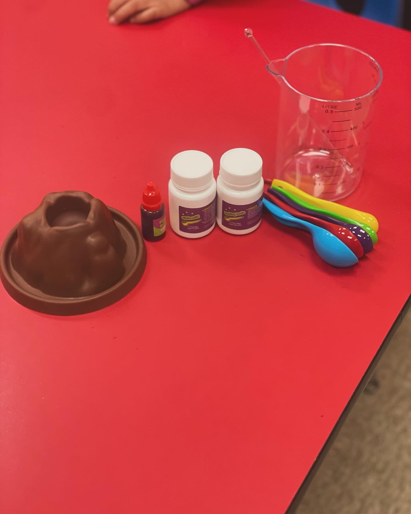 Volcano science experiment materials laid out on a table: citric acid, baking soda, food coloring, and measuring spoons